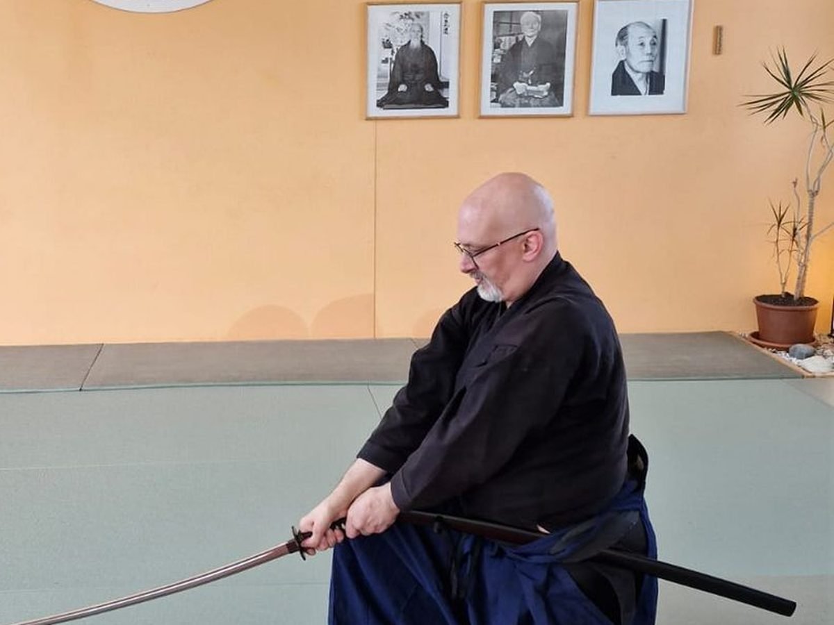 Pratiquant d'Iaïdo en posture à genoux, sabre dégainé, dans le dojo